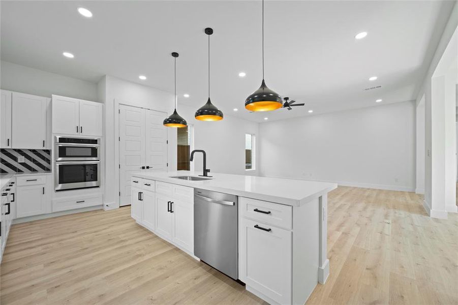 Kitchen with appliances with stainless steel finishes, light countertops, recessed lighting, white cabinets, and a center island with sink
