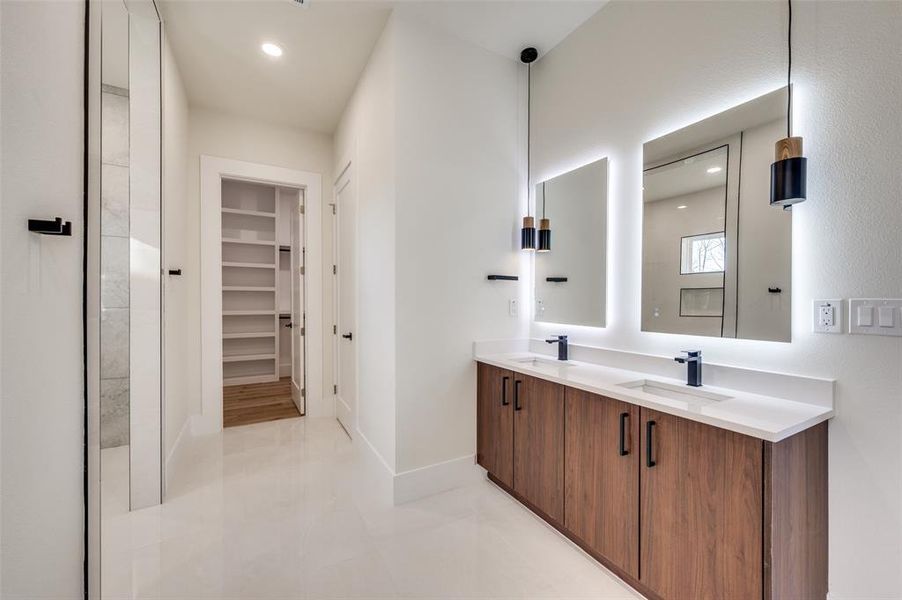 Dual vanity with wood-finish cabinetry, white countertops, and backlit mirrors