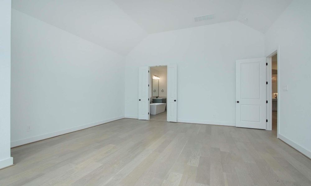 Unfurnished bedroom with light wood-type flooring, lofted ceiling, and ensuite bathroom