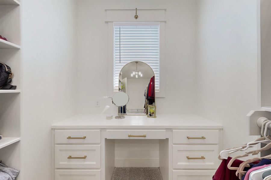 Primary walk in closet with a private built in vanity with lots of natural light, built in drawers at the other end and shoe racks.