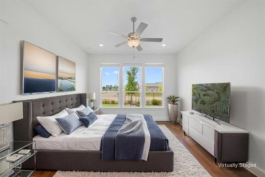 Brightly lit room featuring three large windows, wood-finish flooring, a vaulted ceiling, and a ceiling fan with integrated lighting