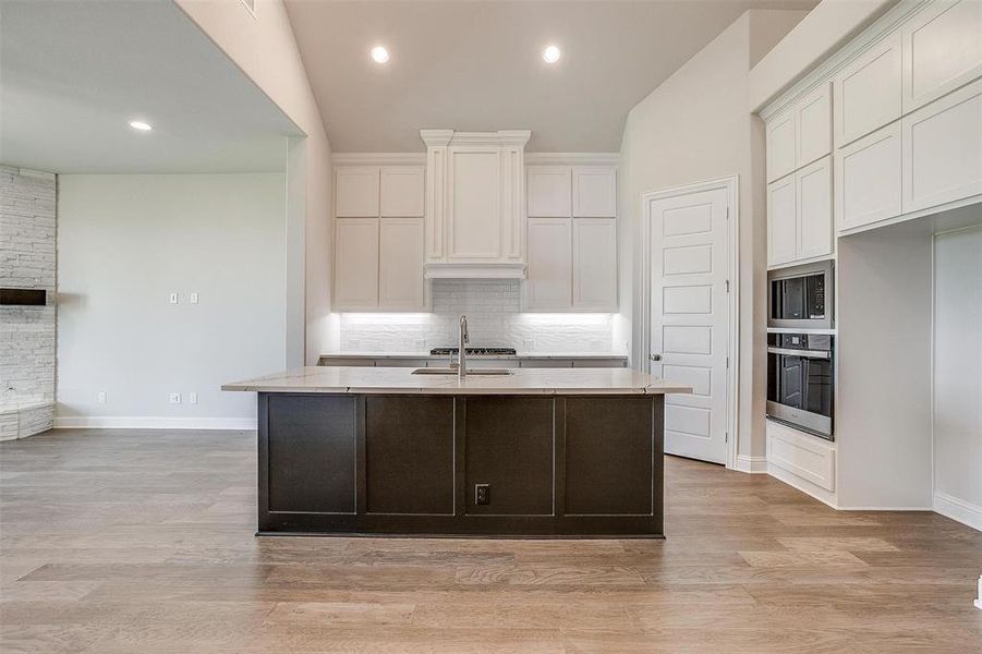 Kitchen with a kitchen island with sink, light hardwood / wood-style flooring, white cabinetry, stainless steel appliances, and vaulted ceiling