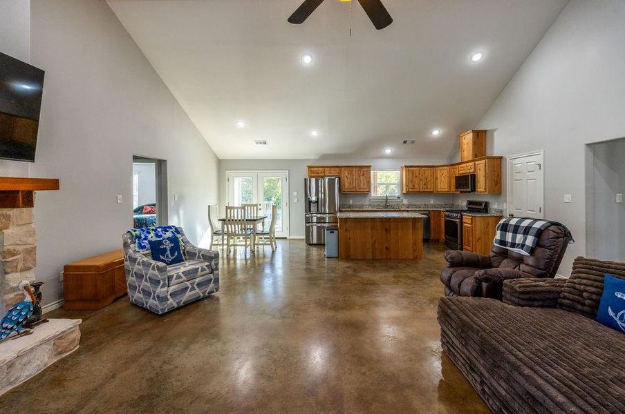 Living area with high vaulted ceiling, finished concrete floors, recessed lighting, a ceiling fan, and a fireplace