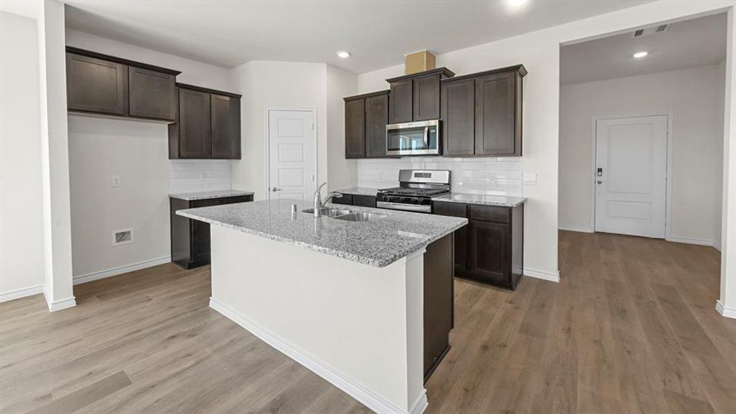 Kitchen featuring wood-finish flooring, dark cabinetry, white subway tile backsplash, and light-toned speckled countertops