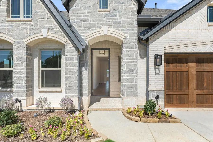 Stone and brick home entrance with arched front door, wood garage door, and landscaped flower beds