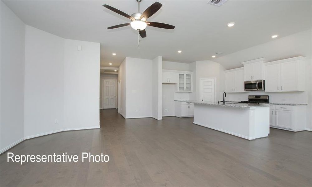 Kitchen with white cabinets, a center island with sink, dark wood-type flooring, appliances with stainless steel finishes, and light stone countertops