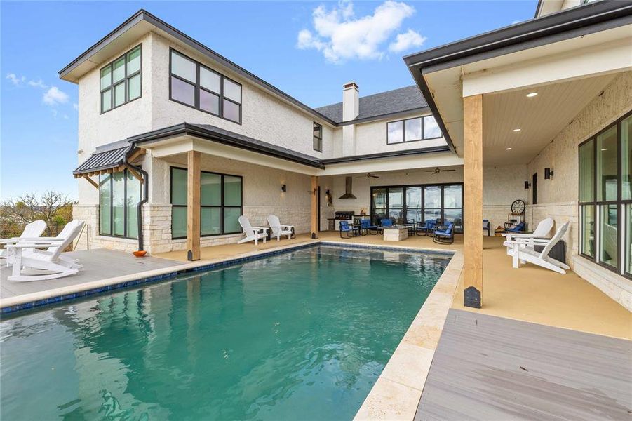 Back of property with a patio area, stucco siding, a chimney, an outdoor pool, and stone siding