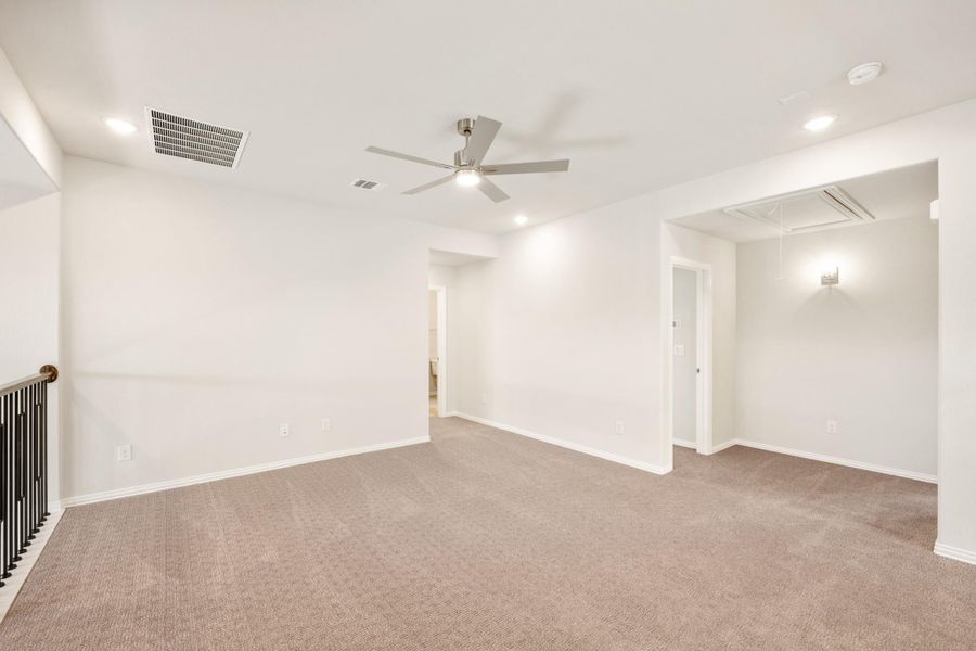 Empty upstairs loft or bonus room with beige carpet, ceiling fan, and staircase railing visible Empty upstairs loft or bonus room with beige carpet, ceiling fan, and staircase railing visible
