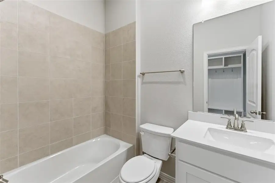 This bathroom features a bathtub with light-colored tile surround, a toilet, and a vanity with a white countertop and an undermount sink
