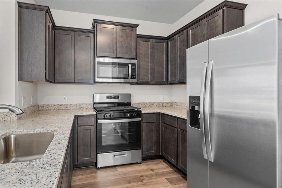 Kitchen featuring stainless steel appliances, dark brown cabinets, light wood-style flooring, and light stone countertops