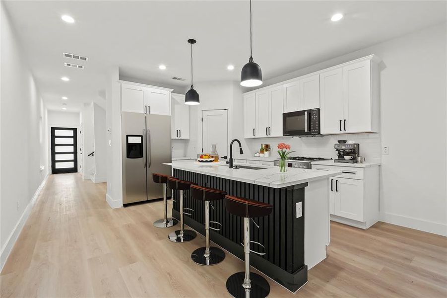 Kitchen with a breakfast bar area, stainless steel refrigerator with ice dispenser, white cabinetry, an island with sink, and recessed lighting