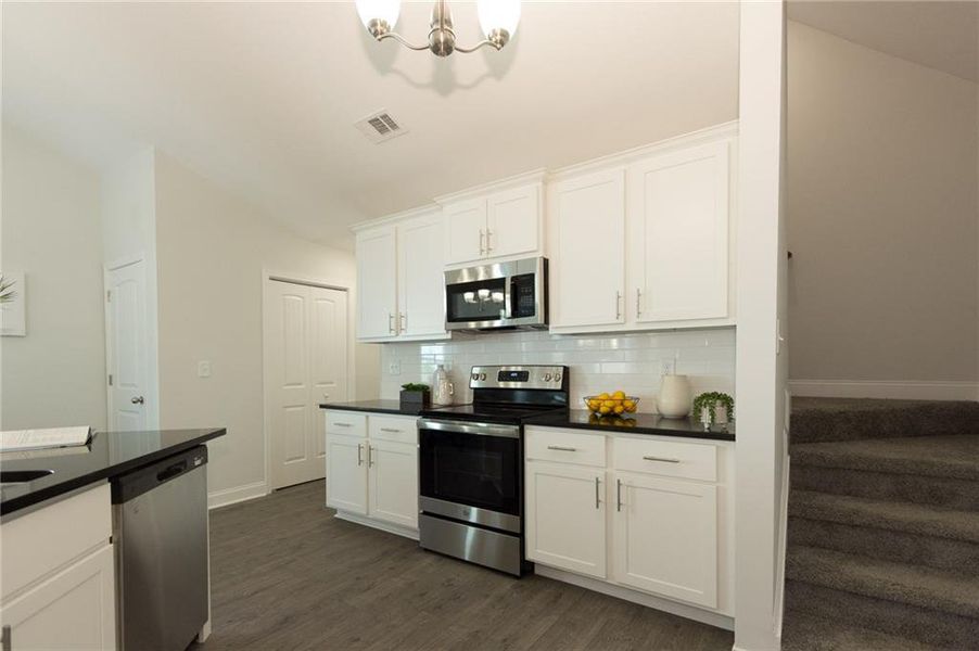 Kitchen featuring a notable chandelier, stainless steel appliances, white cabinets, backsplash, and dark hardwood / wood-style floors