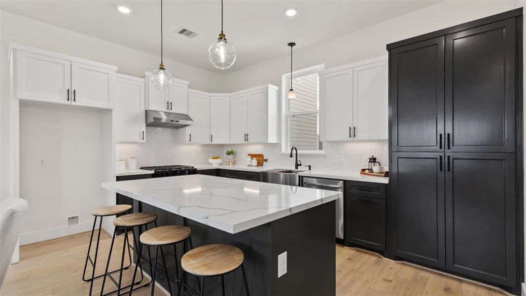 Modern kitchen featuring whitecountertops, a central island withseating, sleek dark cabinetry,stainless steel appliances, andpendant lighting.