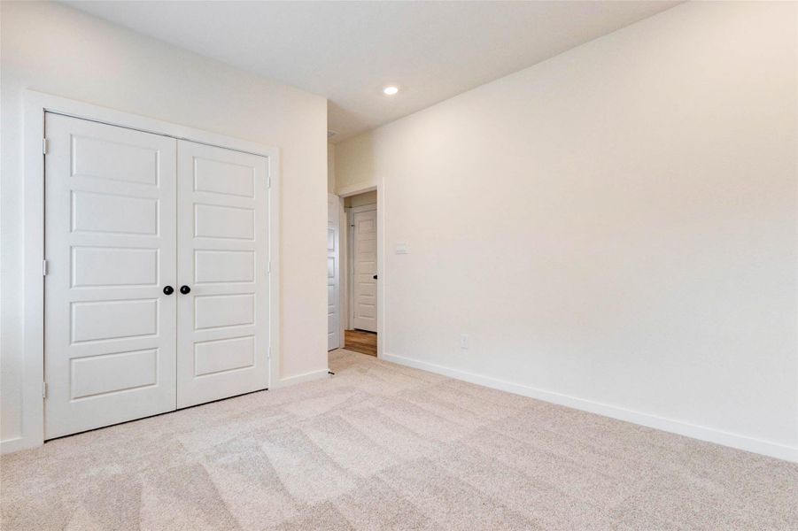 This well-sized secondary bedroom features soft carpeting, neutral tones, and a large closet with double doors for convenient storage. The clean design and natural light create a comfortable and versatile space, perfect for guests, family members, or a home office. Thoughtfully designed, this room adapts easily to a variety of needs.