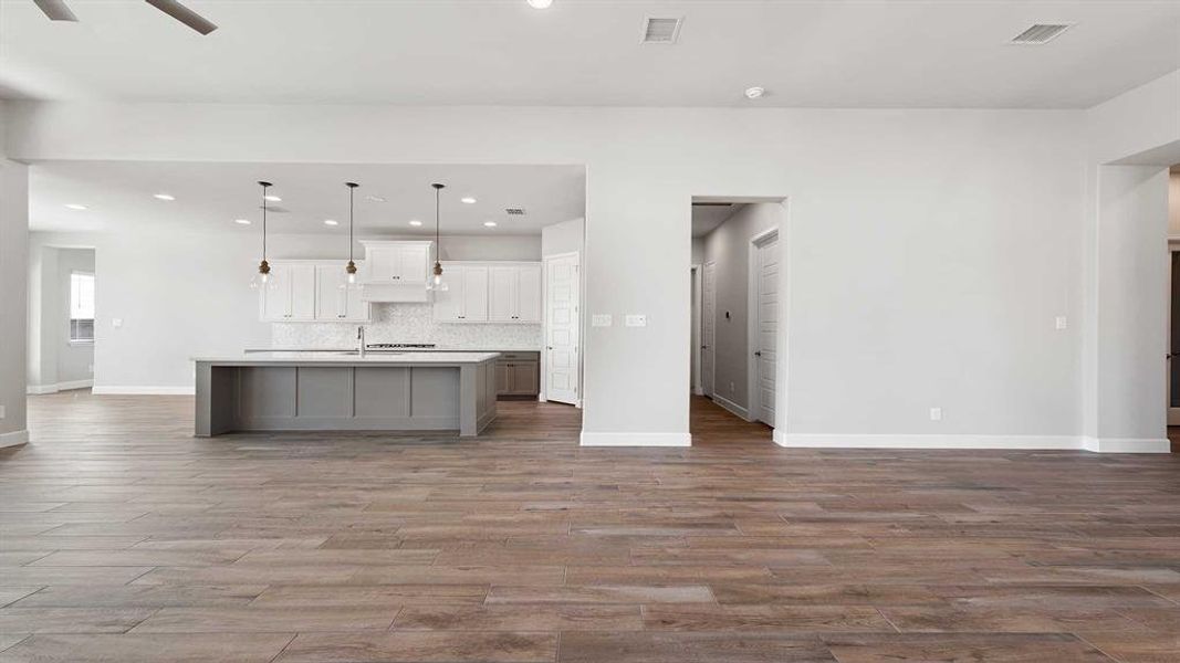 Kitchen with tasteful backsplash, a large island with sink, white cabinetry, wood-type flooring, and decorative light fixtures