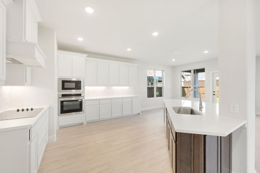 Open kitchen with white cabinets, stainless steel appliances, island with sink, and light wood floors