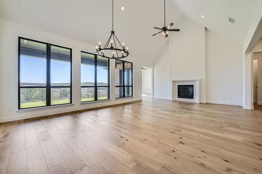 Unfurnished living room with ceiling fan with notable chandelier, high vaulted ceiling, and light wood-type flooring