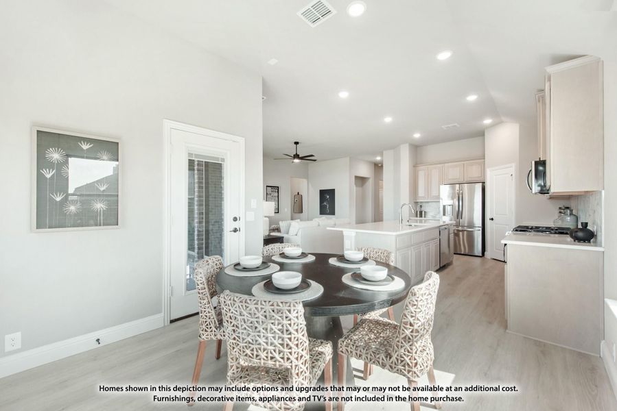 Open-plan dining area with round table, leading to white kitchen with island and stainless steel appliances on light hardwood floors. Open-plan dining area with round table, leading to white kitchen with island and stainless steel appliances on light hardwood floors.