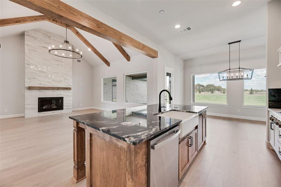 Kitchen featuring a chandelier, pendant lighting, beam ceiling, a center island with sink, and brown cabinetry