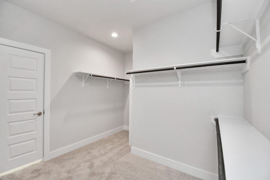 Walk-in closet that epitomizes luxury and practicality. This generously sized space features built-in shelving, offering abundant room for impeccable organization. High ceilings and recessed lighting create a bright and welcoming ambiance. Sample photo of completed home with similar floor plan. Actual colors and selections may vary.