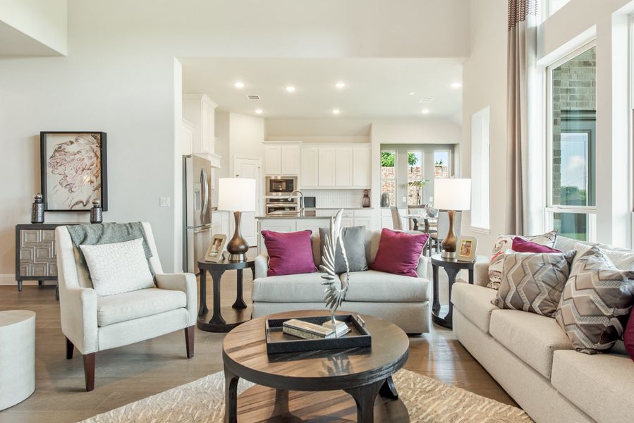 Open-concept living room with neutral sofas, purple accent pillows, and kitchen visible in background Open-concept living room with neutral sofas, purple accent pillows, and kitchen visible in background