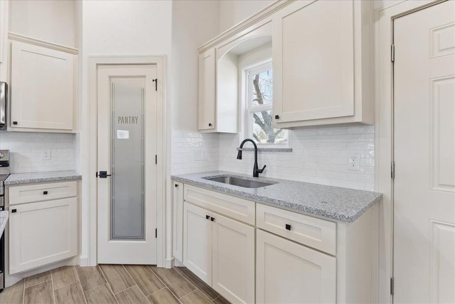 Kitchen featuring sink, light hardwood / wood-style flooring, decorative backsplash, light stone counters, and white cabinetry