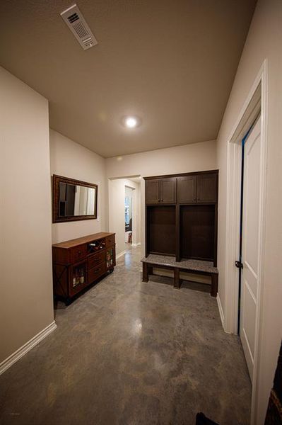 This photo shows a well-lit mud room/hallway with polished concrete floors. It features a wooden console with a mirror above and a built-in bench with storage cubbies. The space leads to another room, offering a functional and welcoming entry or transition area.