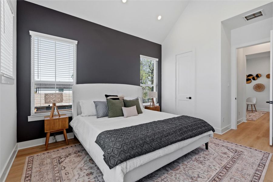 A dramatic vaulted ceiling provides significant vertical volume to this primary suite. The deep charcoal accent wall creates a bold, structural focal point against the crisp white surfaces.