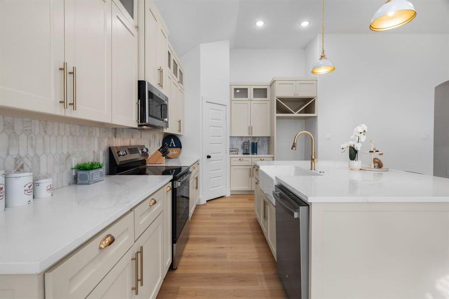 Kitchen with appliances with stainless steel finishes, a kitchen island with sink, glass insert cabinets, light stone countertops, and recessed lighting