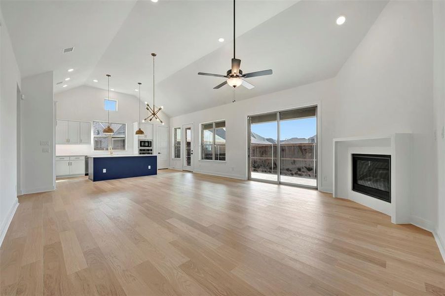 Unfurnished living room with recessed lighting, a glass covered fireplace, light wood-style floors, lofted ceiling, and a ceiling fan Unfurnished living room with recessed lighting, a glass covered fireplace, light wood-style floors, lofted ceiling, and a ceiling fan