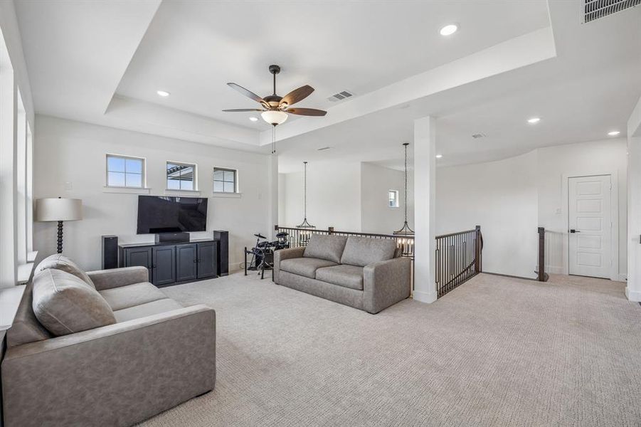 Living area with a raised ceiling, ceiling fan, light colored carpet, and recessed lighting