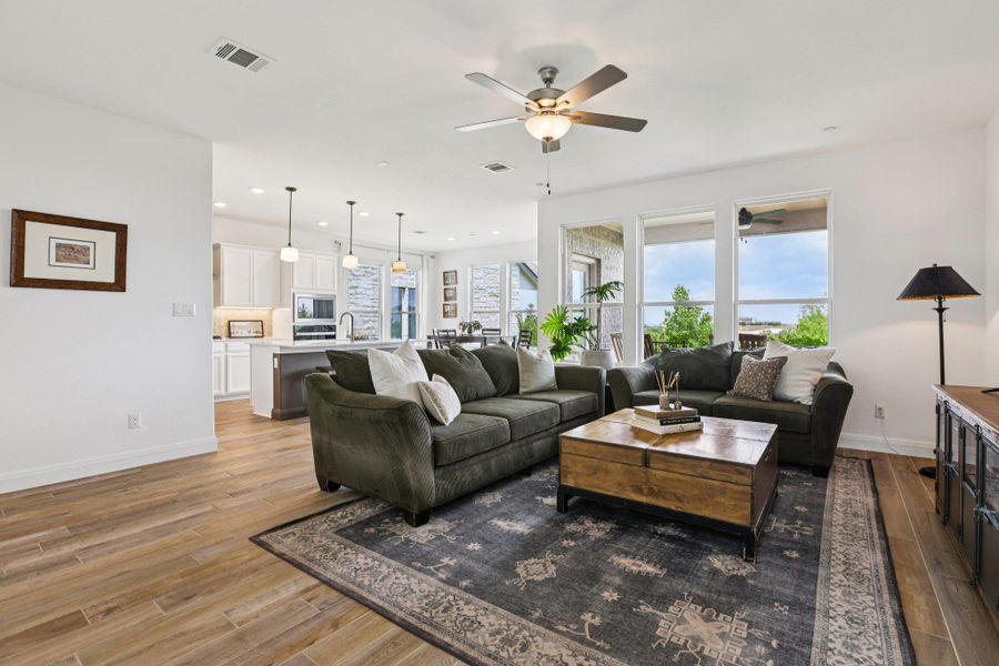 Living area featuring hardwood flooring, an overhead fan with integrated lighting, and large windows providing views of the outdoors