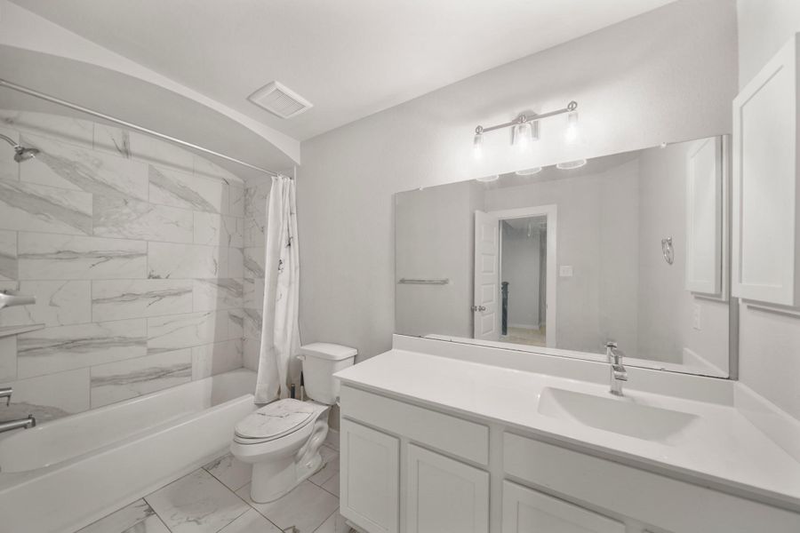 Secondary bathroom with tile floors, granite countertops and backsplash, a large mirror, and a shower/tub combo.