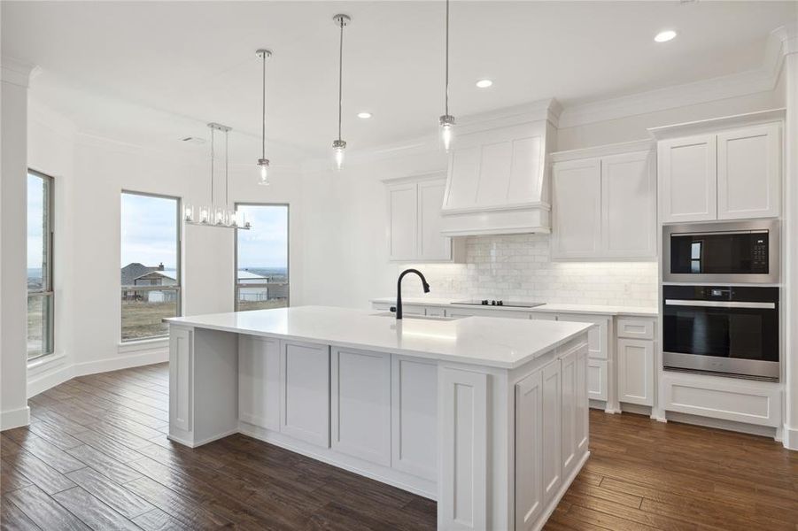 Kitchen with hanging light fixtures, stainless steel appliances, white cabinetry, dark hardwood / wood-style floors, and an island with sink