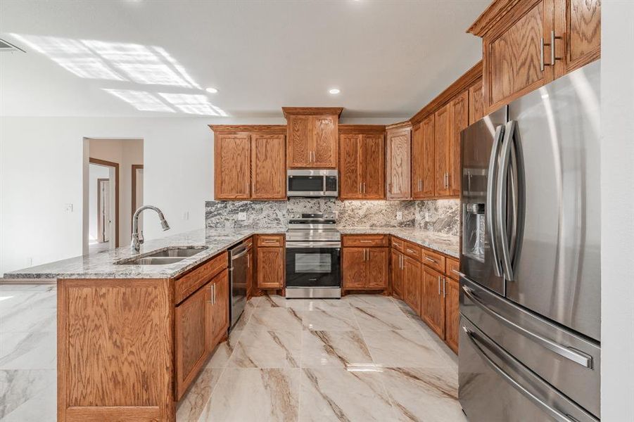 Kitchen featuring marble finish floor, brown cabinets, appliances with stainless steel finishes, a sink, and a peninsula