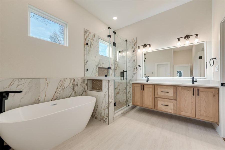 Primary Bathroom with a freestanding bath, double vanity, a marble finish shower, tile walls, and a wainscoted wall