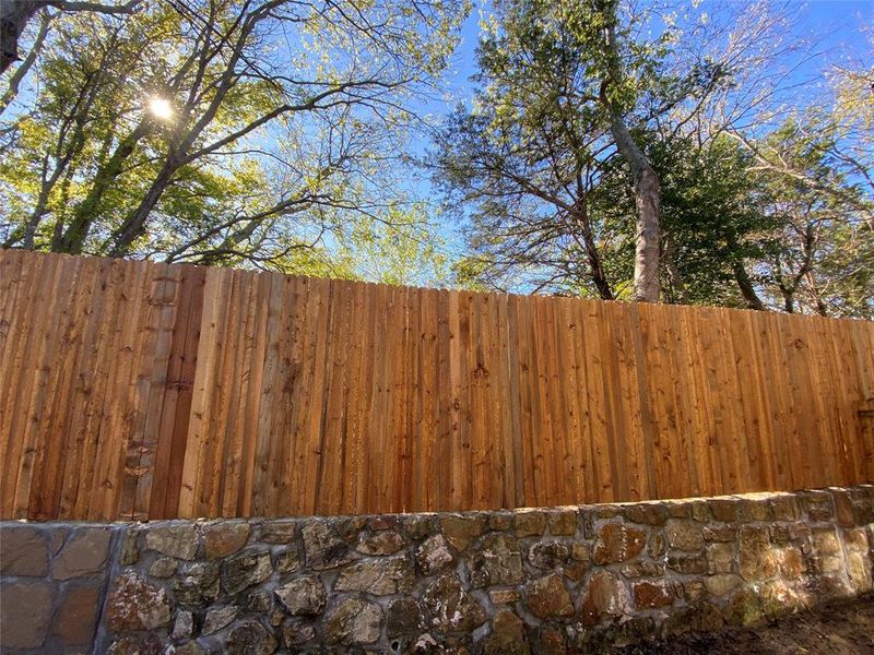 View of private side yard with tall fence and large trees.