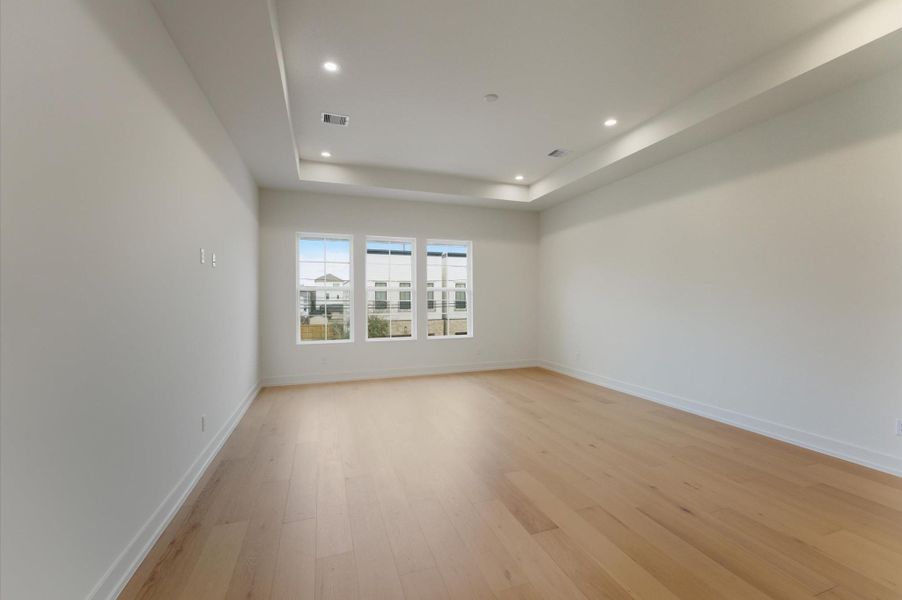 Primary bedroom with a tray ceiling and abundant natural light.