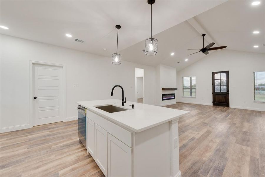 Kitchen with an island with sink, sink, decorative light fixtures, white cabinets, and light hardwood / wood-style floors