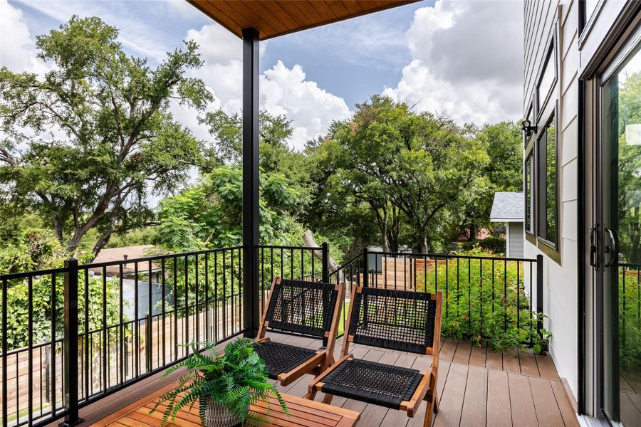 The covered deck area, framed by an elegant iron railing, offers a sheltered outdoor retreat, perfect for relaxing or entertaining in any weather.