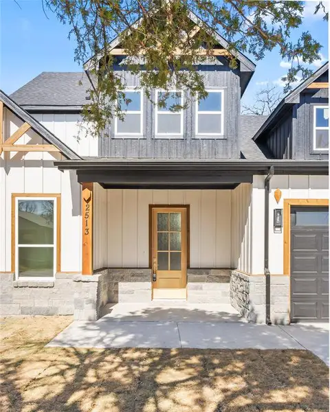 Modern farmhouse with a shingled roof, a porch, and a garage Modern farmhouse with a shingled roof, a porch, and a garage