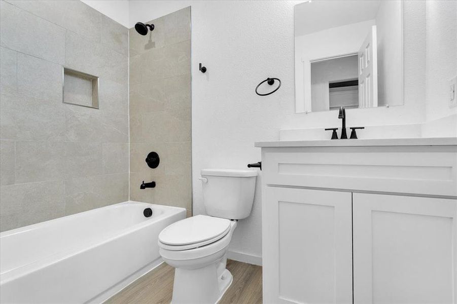 Full bathroom with hardwood / wood-style flooring, tiled shower / bath, vanity, and toilet