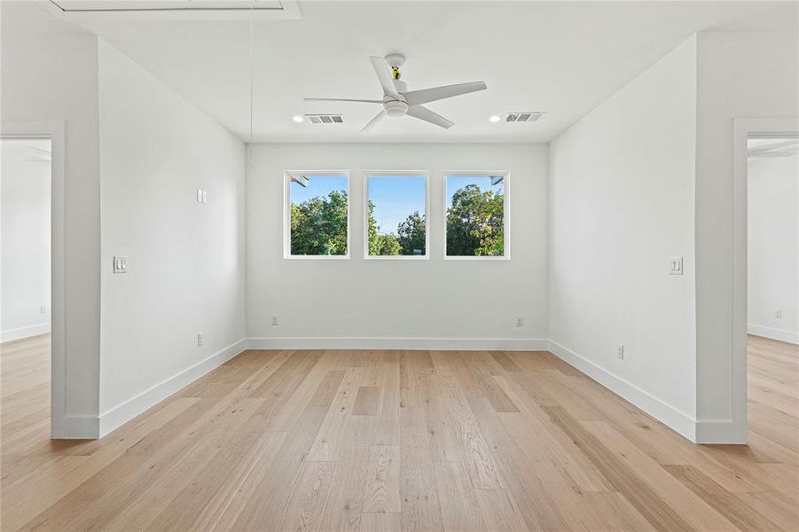 Unfurnished room featuring attic access, light wood-type flooring, and a ceiling fan