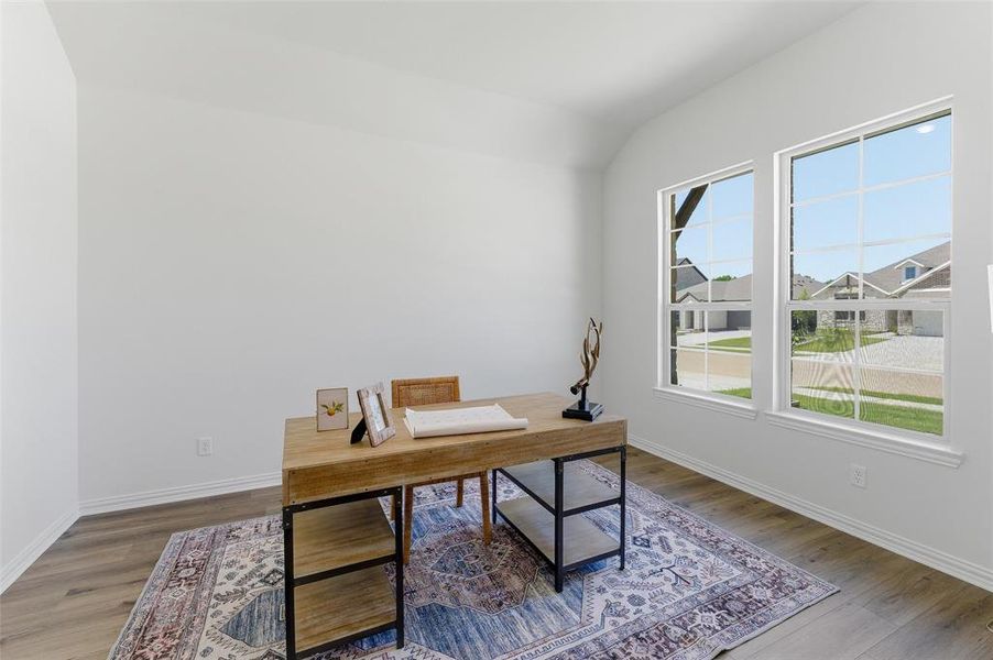 Room featuring two large windows with grid muntins, wood-finish flooring, white baseboards, and vaulted ceilings