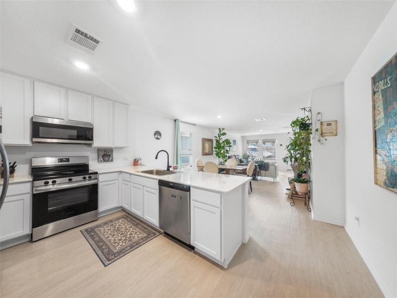 Kitchen featuring stainless steel appliances, a peninsula, open floor plan, white cabinets, and light wood-style floors