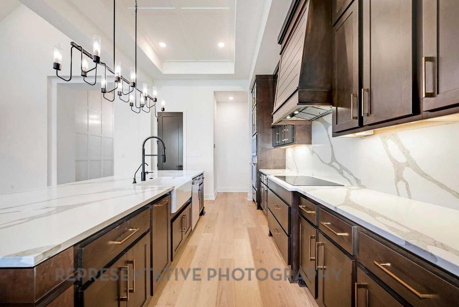 Kitchen featuring dark brown cabinets, light stone counters, light wood-style flooring, decorative light fixtures, and premium range hood Kitchen featuring dark brown cabinets, light stone counters, light wood-style flooring, decorative light fixtures, and premium range hood