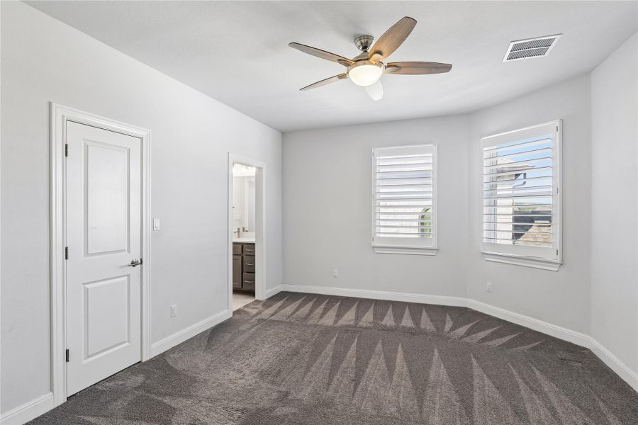 A well-lit bedroom features plush carpeting and multiple windows for abundant natural light.