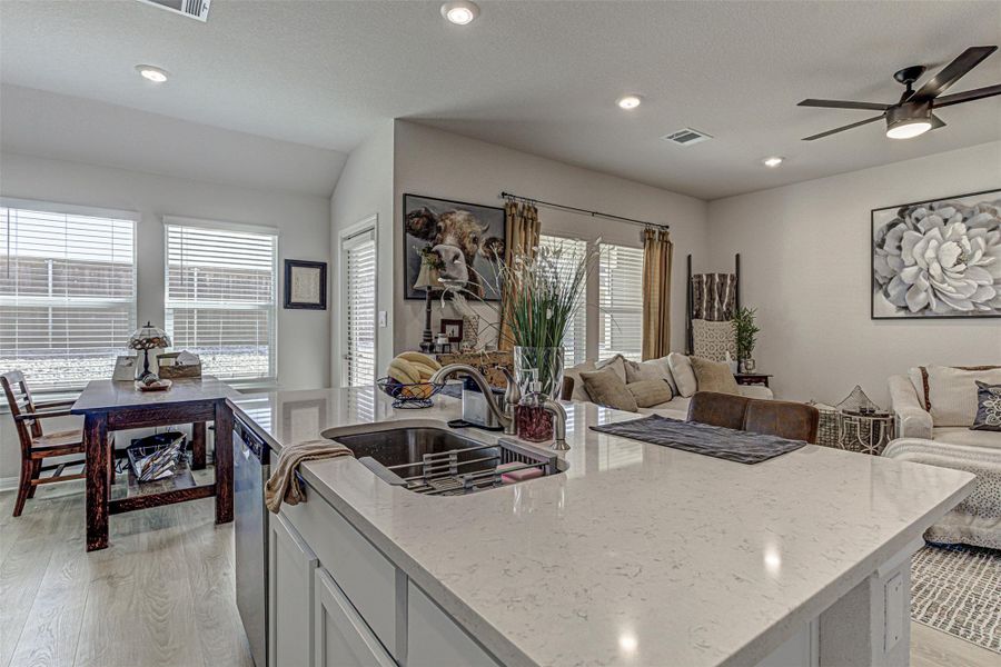 Kitchen featuring light wood-type flooring, light stone counters, a ceiling fan, a kitchen island with sink, and white cabinets