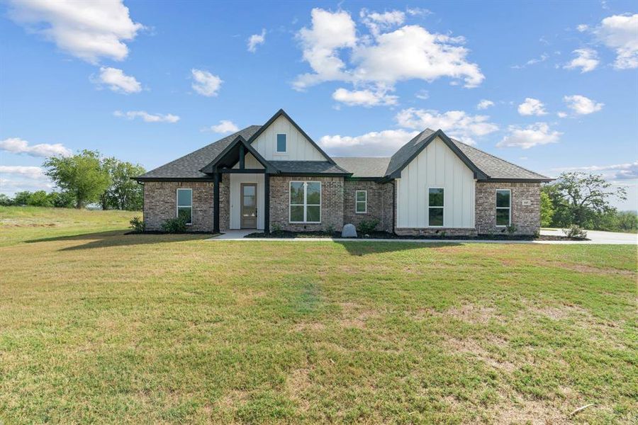 Property entrance with board and batten siding, brick siding, a shingled roof, and a yard