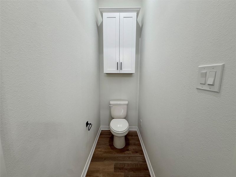 Private water closet featuring wood-finish flooring, white walls, and a built-in white cabinet with black hardware